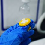 Mão enluvada segura um filtro de seringa em um laboratório.