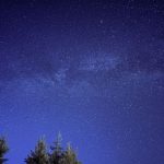 Meteoro riscando o céu estrelado acima da silhueta de uma floresta