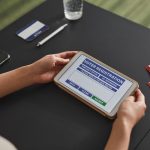 Pessoa utiliza um tablet durante um processo de registro eleitoral em um local de votação.