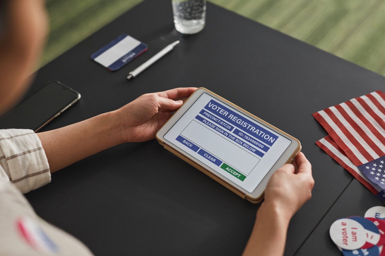 Pessoa utiliza um tablet durante um processo de registro eleitoral em um local de votação.