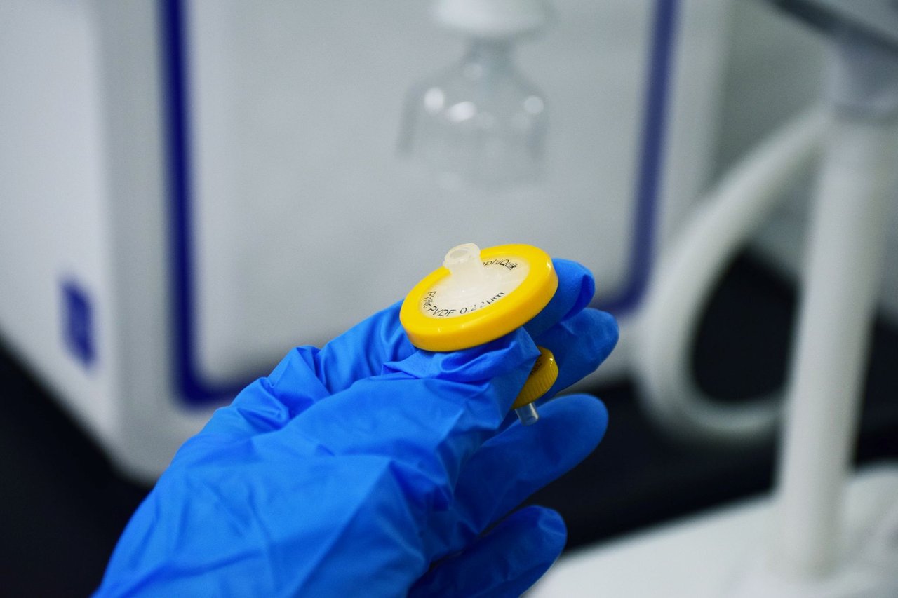 Mão enluvada segura um filtro de seringa em um laboratório.
